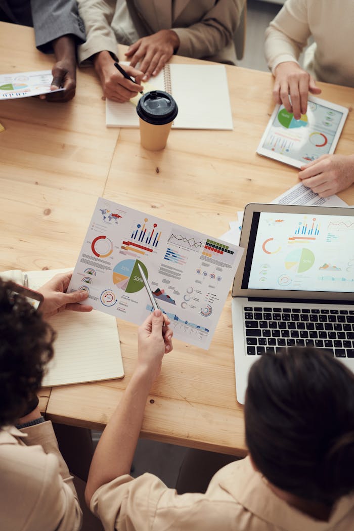 Los compañeros colaboran en el análisis de datos en una reunión de equipo con gráficos y un ordenador portátil.