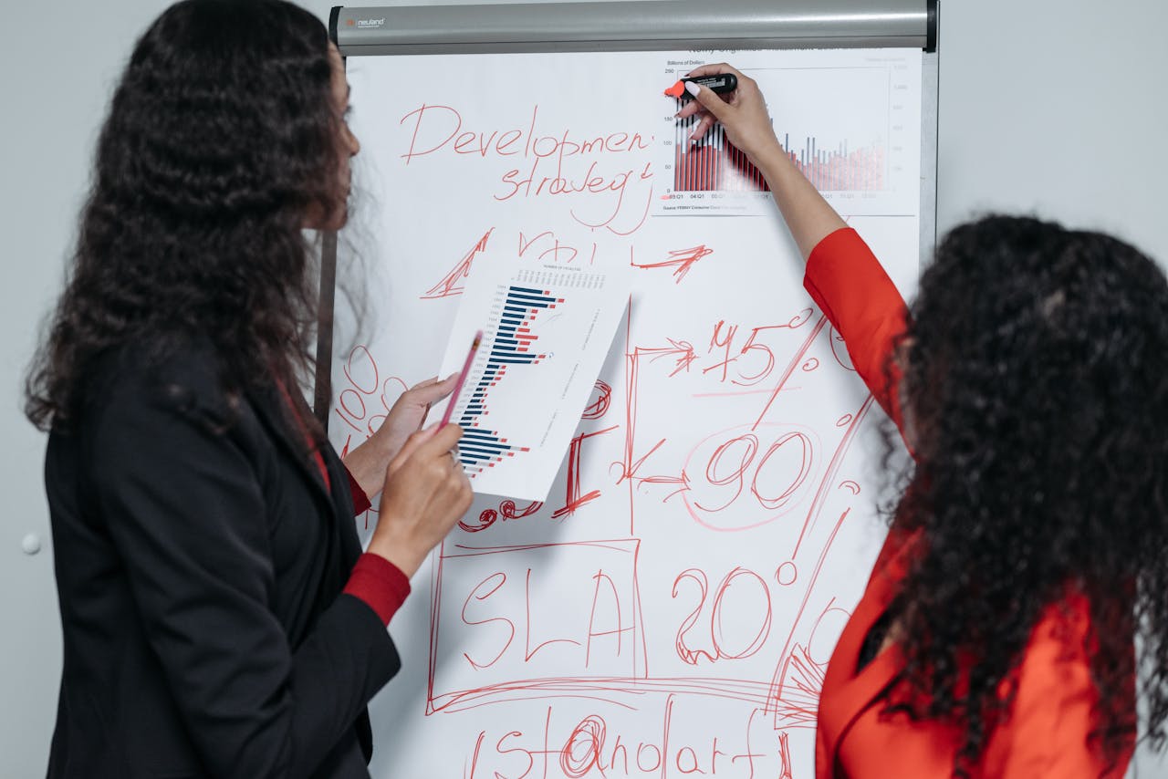 our-mission Two professional women discuss and strategize on business development in a modern office setting.